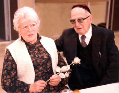 Andree Salomon, holding a rose, and her husband sitting beside her in a suit