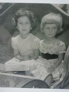 Marjorie Agosin and her sister as children, wearing dresses and sitting in a small sled or cart