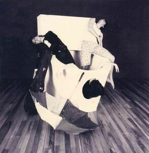 Three dancers flopped in and on top of a large white cylinder, with a guitar case and an open umbrella leaning against it