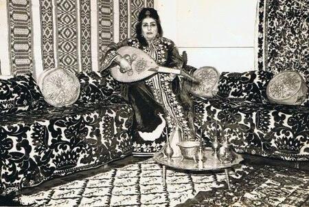 Zohra El Fassia holding an instrument, wearing a dress gifted to her by King Mohammed V, in an ornate room, likely the museum exhibit on North Africa 