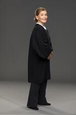 Judy Sheindlin smiling and standing in her judicial robes in front of dark backdrop