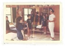 Campers standing at ends of their bunks with camp mother on the right side in all white