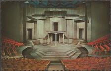 A drawing of a stage surrounded by red seats, with a grey, cubist set design featuring three doorways, several staircases, and a balcony held up by five pillars