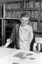 Tatyana Grosman, standing at a table in front of a bookshelf