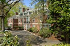 A large brick building with a wide driveway, surrounded by trees