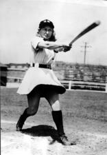 Thelma Eisen swinging a bat, wearing a skirted baseball uniform and a hat reading "GR"