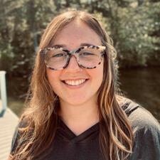 Headshot of Emma Mair with shoulder-length light brown hair and tortoiseshell glasses, posing in front of trees