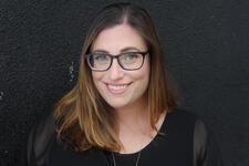 Woman with long brown hair, dark rimmed glasses and dark shirt