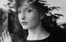 Black and white photograph of woman looking out a window with her hand against the glass.