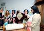 Woman removes cover from Torah scroll at bimah as group of women looks on