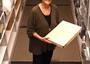 Woman standing holding large box, library shelves in background