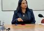 Woman with dark hair wearing dark suit sits at conference table; microphone point in her direction