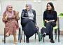 Photo of three women sitting side by side; the woman on the left and in the center have their heads covered, the woman on the right is dressed in black