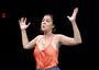 Woman in a theatrical performance, wearing orange tank stop and with arms in "hands up" position