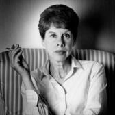 A portrait of anita Brookner, sitting in an armchair with her arms crossed, holding a cigarette