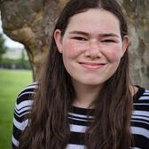 Photo of Ilana Drake, standing in front of a tree wearing a striped shirt.