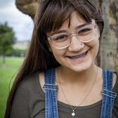 Photo of Eleanor Harris, in front of a tree wearing a grey shirt and overalls.