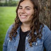 Photo of Ari Fogel, in front of a tree wearing a black shirt and a jean jacket