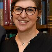 Mayim Bialik standing in front of a bookshelf with Jewish books