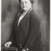 Portrait of Rosa Manus standing to the side of a desk with hand on two books 