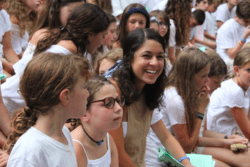 Camp counselor surrounded by campers, all wearing white. Sitting on benches during services.