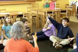 Allyson Mattanah, her back to the camera, teaches young students who are engaged and raising their hands.