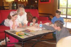 Grandmother coloring on paper with her grandchildren. They sit on and around a red couch.