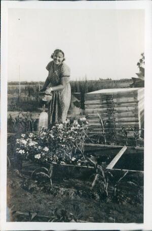 A smiling woman stands behind a planter box watering flowers