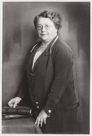 Portrait of Rosa Manus standing to the side of a desk with hand on two books 