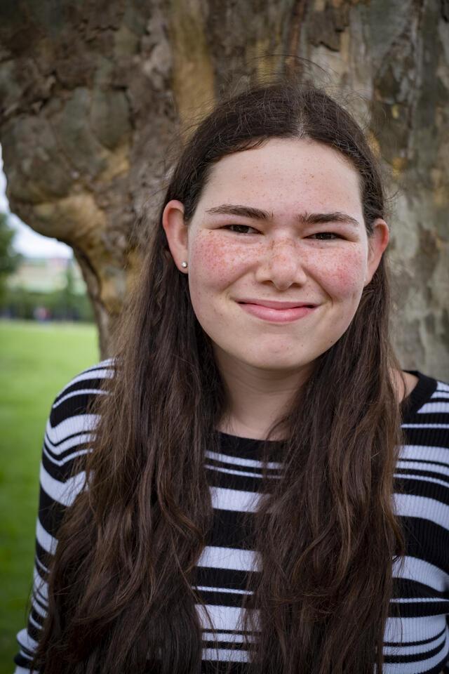 Photo of Ilana Drake, standing in front of a tree wearing a striped shirt.