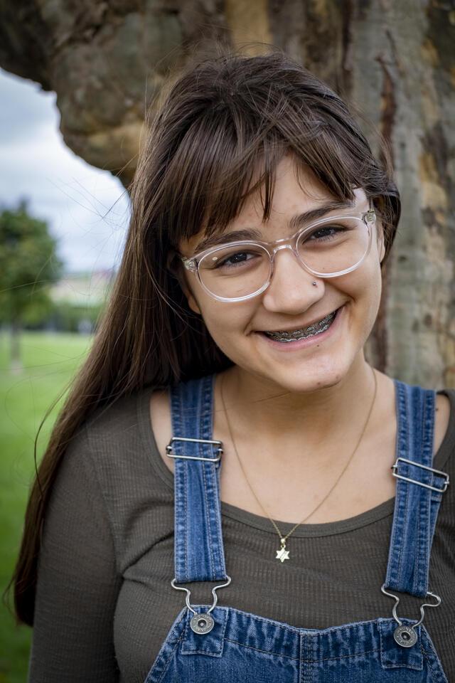 Photo of Eleanor Harris, in front of a tree wearing a grey shirt and overalls.