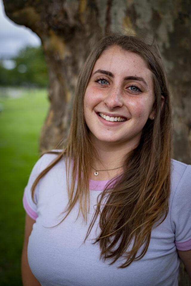 Photo of Ella Plotkin-Oren, in front of a tree wearing a white shirt with pink detailing.