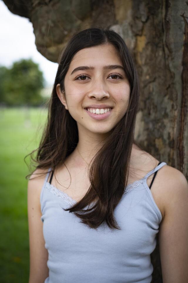 Photo of Maddy Pollack, in front of a tree wearing a grey shirt.