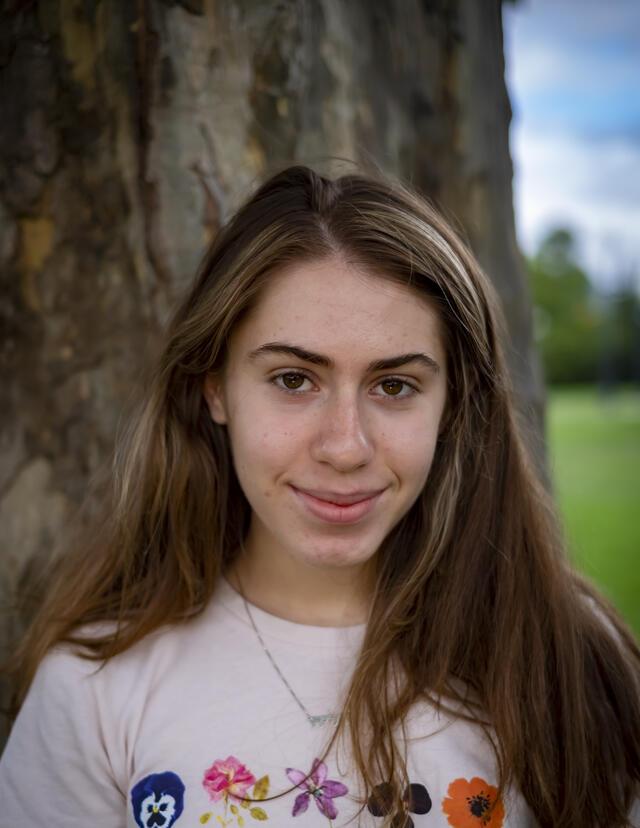 Photo of Dahlia Soussan, in front of a tree wearing a white shirt with an illustrated flower pattern.