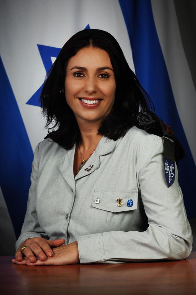 Miri Regev seated in front of an Israeli flag, wearing decorated uniform.