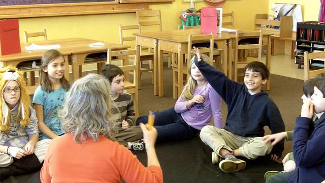 Allyson Mattanah, her back to the camera, teaches young students who are engaged and raising their hands.