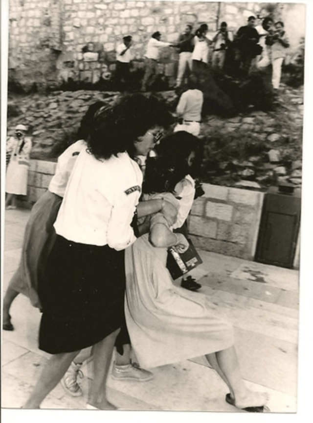 A women being in struggle while being grabbed by the arms by officials