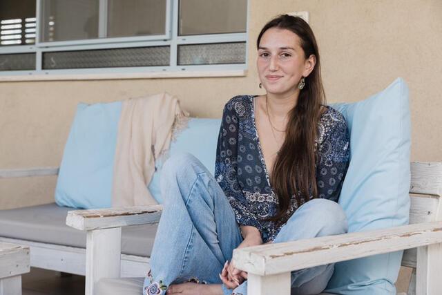 Young woman sitting in chair with long brown hair, long sleeve top and jeans