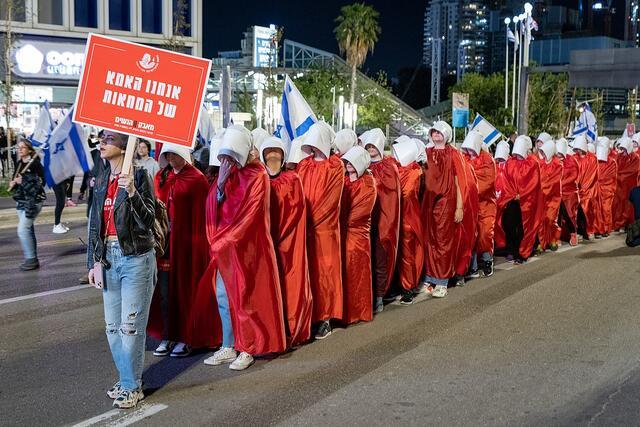 Women in red robes and white caps marching in protest, evoking the Handmaid's Tale