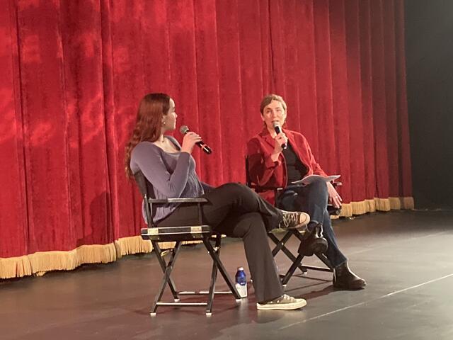 Judith and Ma'ayan Rosenbaum sitting on a stage with microphones, red curtain behind them