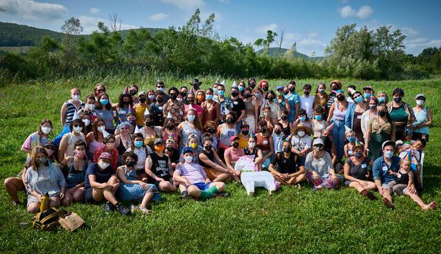 Large group of people sitting on grass, hills in background. 