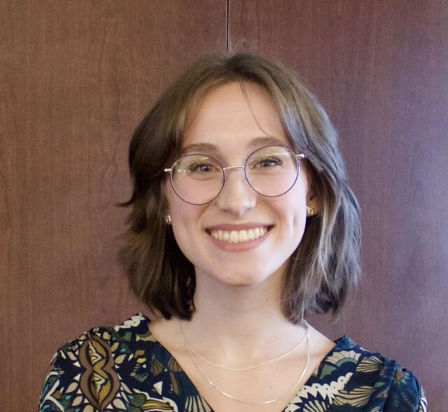 Woman with chin-length brown hair and glasses posing against a dark background